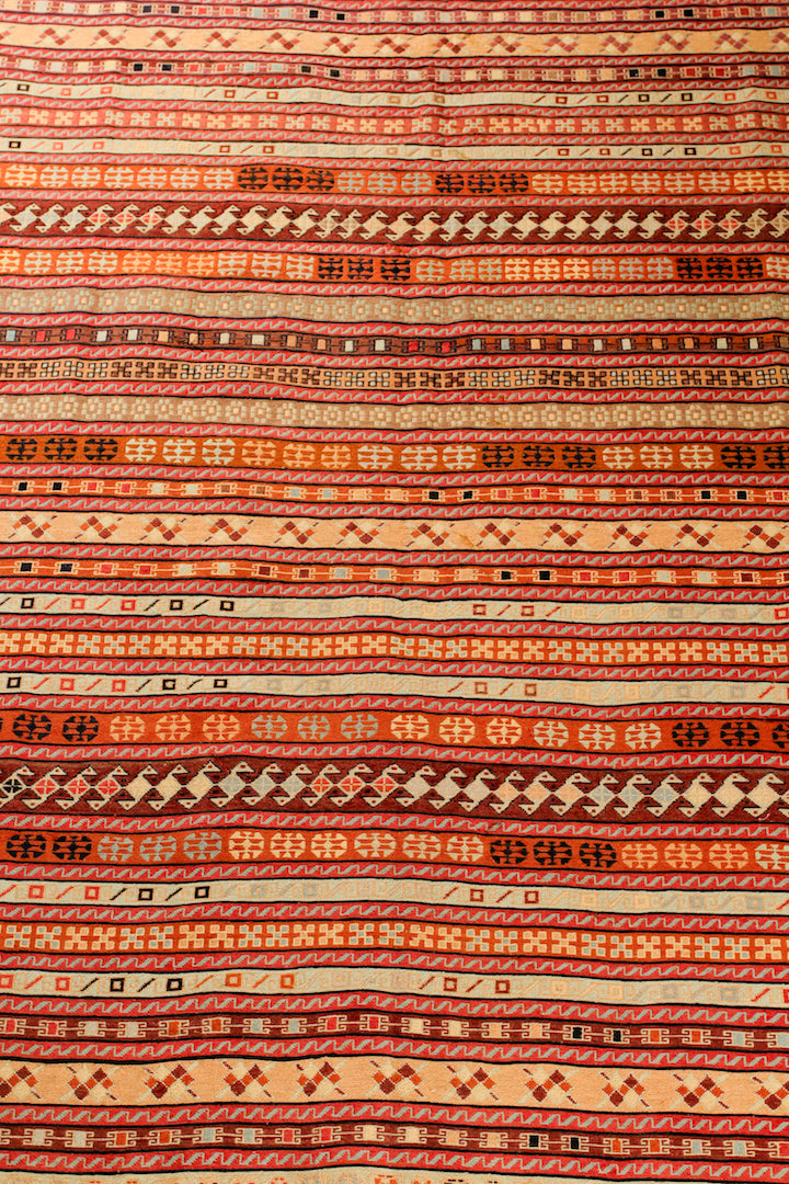 A 6.5 by 9.5 feet shirazi wool kilim. The colours mainly include orange, brick, brown, beige and tan.