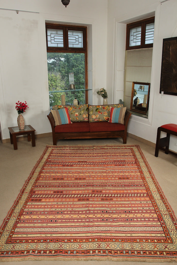 A 6.5 by 9.5 feet shirazi wool kilim. The colours mainly include orange, brick, brown, beige and tan.