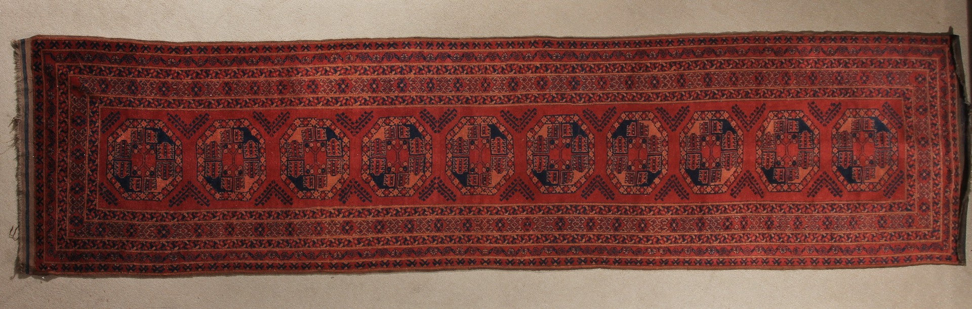 A 2.5 feet by 10 feet turkoman wool rug. The colours used are deep red,rust and black.