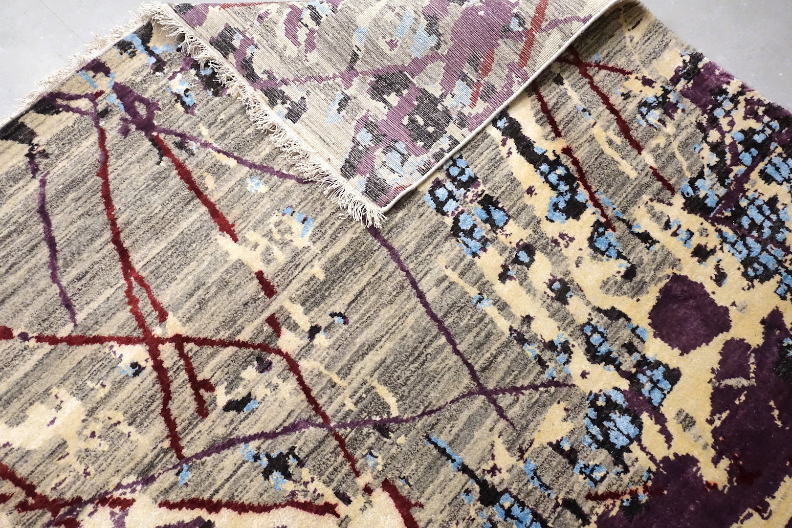 The rug/carpet consists of modern design. With a striped black and white based. Purple and Blue sprawled across like ink spread on paper. The rug is 5 feet by 7 feet. 