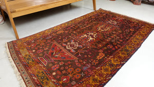 A 3.5 feet by 6.5 feet antique Balochi wool rug, the colours used on the rug are brown, tan, red, green, blue and beige.