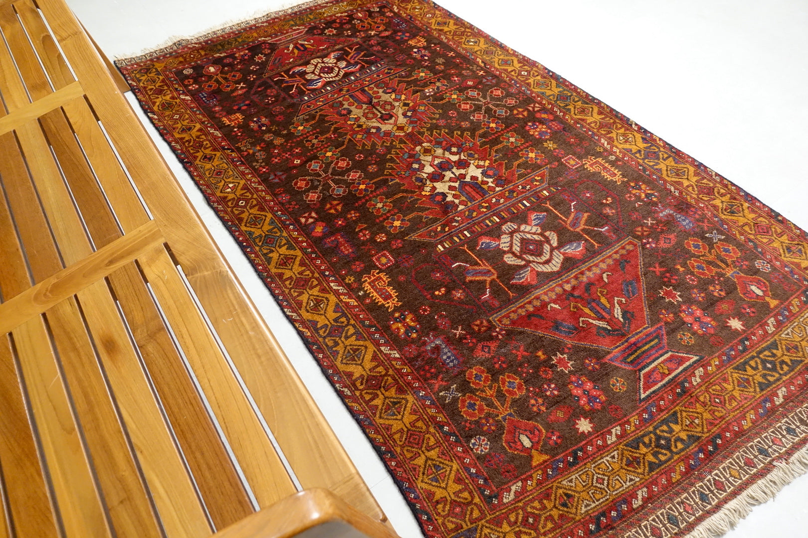 A 3.5 feet by 6.5 feet antique Balochi wool rug, the colours used on the rug are brown, tan, red, green, blue and beige.