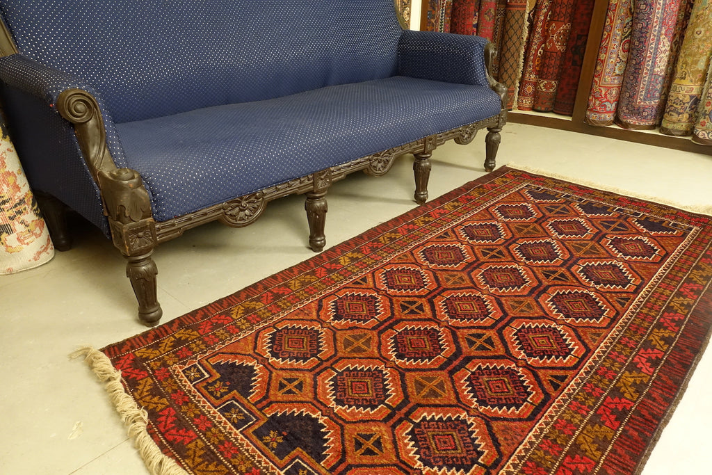 A 3.5 by 6 feet balochi wool carpet, the colours used on the rug are navy blue, orange and pink-red.